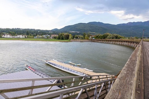 Dragon boats are tied up at a floating dock near a wooden pier, with the city of salmon arm and the