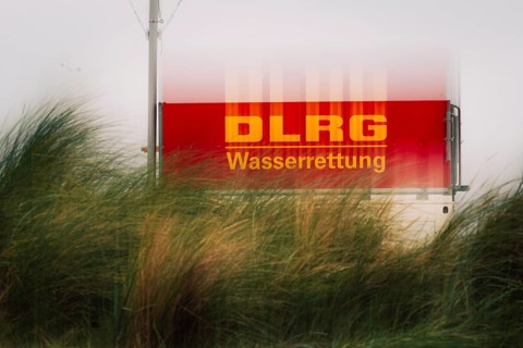 DLRG sign on the coast, red sign with the inscription DLRG Wasserrettung partly covered by high