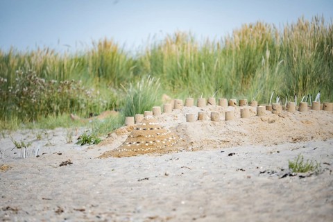 Sandcastle on the beach, small sandcastle in the foreground in front of overgrown dunes with beach