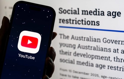 In this photo illustration, a person holds a phone displaying the YouTube app in front of a screen