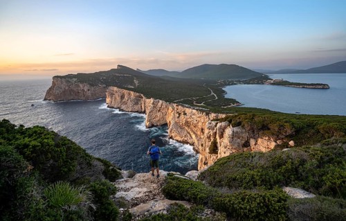 Tourist in front of coastal landscape at sunset, steep cliffs by the sea, cliffs in the evening