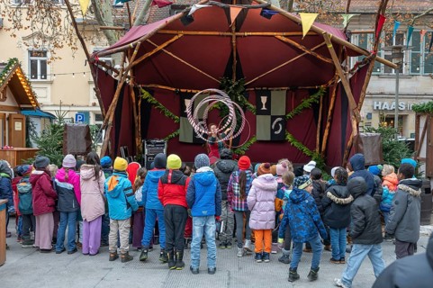A group of children watches an acrobat on stage, Historischer Christmas market am Neustädter church