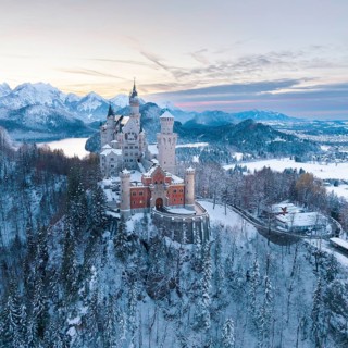 Fairytale castle Neuschwanstein in a wintry landscape with pastel-coloured sky and mountains,