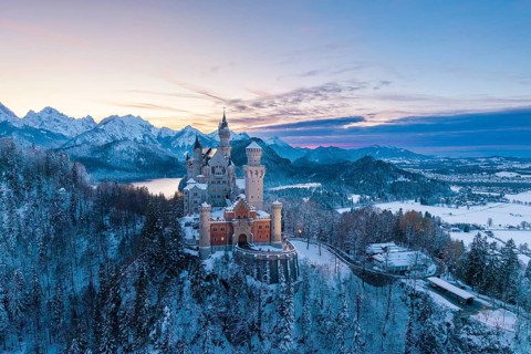 Neuschwanstein Castle in winter at sunset with snow-covered mountains and peaceful atmosphere,