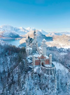 Neuschwanstein Castle in a wintry landscape with snow-covered mountains and blue sky, peaceful
