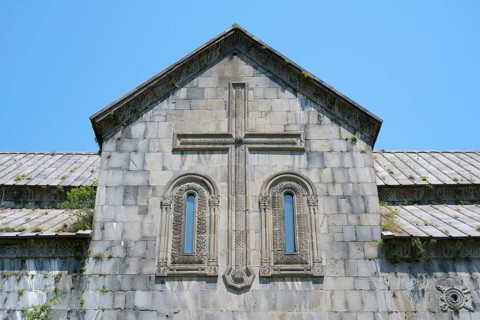 Historic church façade with stone cross and windows under a blue sky, Akhtala monastery, Akhtala