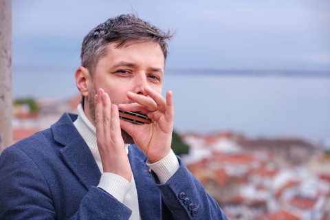 Man musician in a blue blazer and white sweater playing blues on a harmonica with eyes closed,