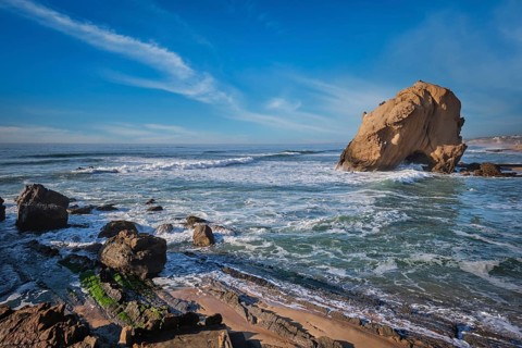 Penedo do Guincho, a large boulder rock arch at Praia da Santa Cruz, Portugal, with ocean waves and