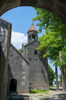 View through an arch of a church with bell tower, surrounded by trees, in shade, Sanahin monastery,