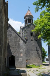 Stone church tower with bell tower, surrounded by trees and shade, blue sky visible, Sanahin