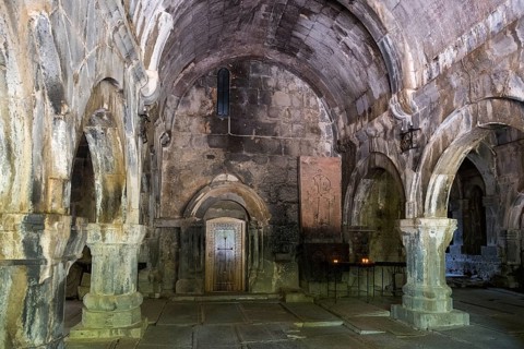 Dark, antique stone hall with arches flanked by glowing candles, Sanahin monastery, Sanahin town,
