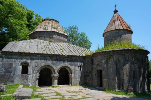 Historic monastery with two domes, overgrown roofs and stone structures under clear skies, Sanahin