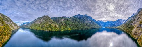 Calm lake with boat surrounded by high mountains and dramatic sky, Germany, Königssee, drone,