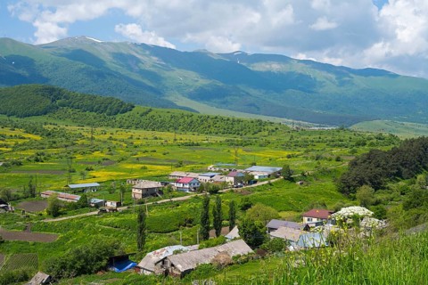 A quiet village in a green valley with mountains and blue sky in the background, Fioletowo,