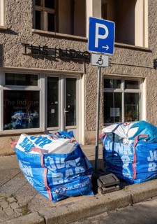 Plastic bags with construction waste lie on the side of the road and block access to a parking