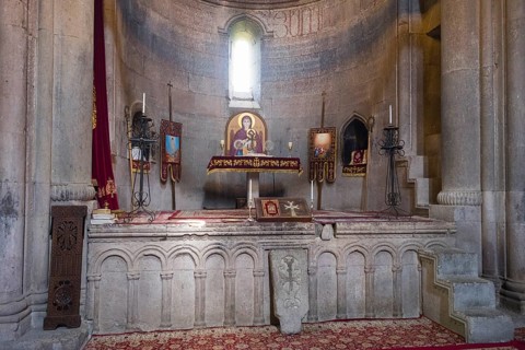 Historic church altar with icons and candles in a stone room, illuminated by windows, Goshavank