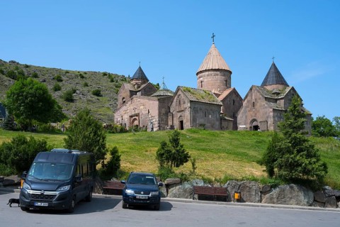 Historic monastery with stone buildings in a mountainous landscape with bright blue sky, Goshavank