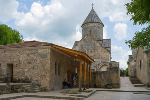 Church building with tower and stone walls, surrounded by trees, in cloudy sky, Haghartsin