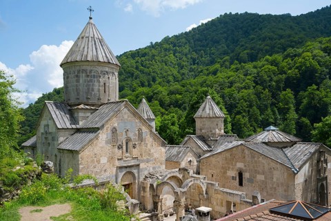 Monastery complex on green hill with towers and stone buildings surrounded by forest, Haghartsin