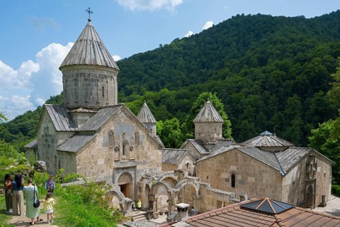 Monastery complex with towers and stone buildings against green mountains and sky background,