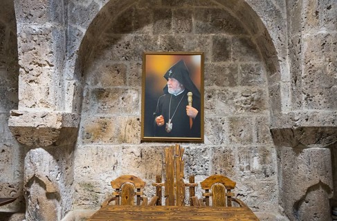 Interior view with painting of a religious motif in front of a stone wall and wooden furniture,