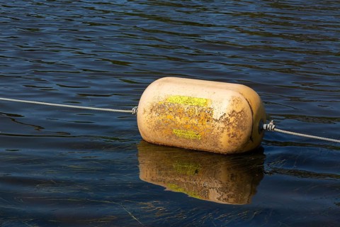 Yellow cautionary navigation buoy on river water surface serving to warn, signal or indicate of a