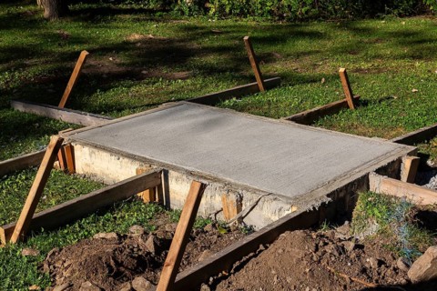 Wooden concrete pouring forms and freshly poured raised concrete base for anchoring a bench in