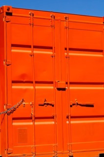 Locked bright fluorescent orange painted metal box shaped shipping container with doors locked