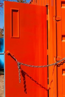 Entrance door kept opened with a chain on bright fluorescent orange painted metal box shaped