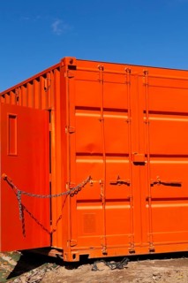Locked bright fluorescent orange painted metal box shaped shipping container with door kept opened