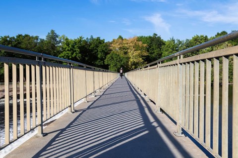 Electric scooter rider on pedestrian walkway on top of water flow control Moulin Neuf dam over Des