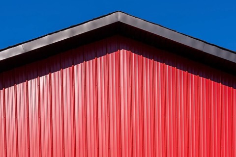 Close-up of building with black metal trim gable roof edge and cladded with red sheet metal siding,