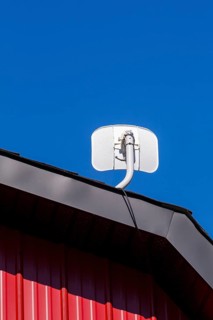 White satellite T.V dish antenna installed on gable roof of building cladded with red sheet metal