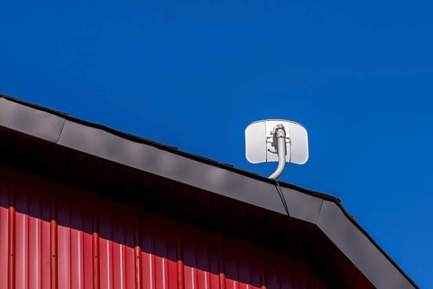 White satellite T.V dish antenna installed on gable roof of building cladded with red sheet metal