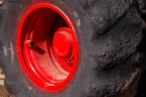 Close-up and rear side view of large heavy duty black rubber tire mounted on red rim on monster