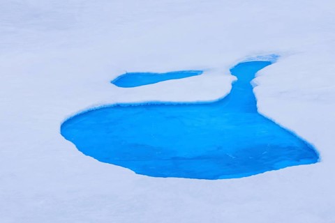 Aerial view over vivid blue water of meltpond / melt pond / meltwater pool on sea ice in the Arctic