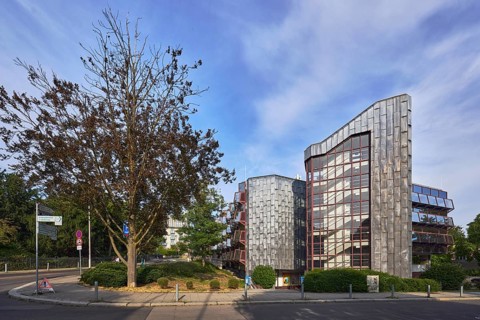 Theatre car park, modern architecture, sidewalk, barrier bollards, trees, bushes, lawn, blue sky,