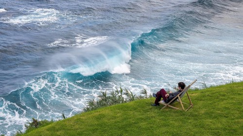 Woman sitting comfortably in deckchair in a meadow and watching waves in the sea, Madeira, Portugal