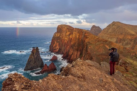 Photographer taking pictures on cliffs, rainbows over sea, volcanic peninsula, Ponta de São