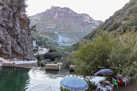 View of a quiet river and road in front of a picturesque mountain panorama with umbrellas, El Kelaa