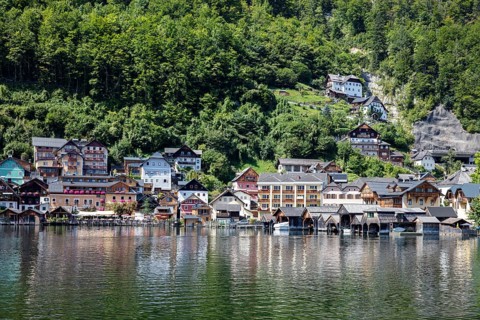 A, Hallstatt, Traditional wooden houses on the shore, surrounded by lush greenery and water,