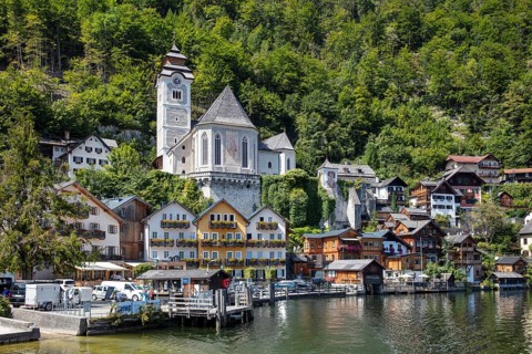 A, Hallstatt, White Church and picturesque houses on the water, surrounded by green mountains,