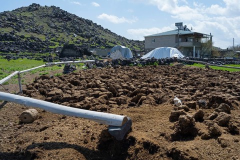 Rural area with hills, rocky soil and farm buildings under blue skies, cow dung to dry, Demirtepe,