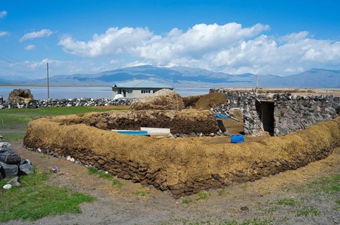 Rustic landscape with traditional clay construction and meadow under clear sky, cow dung to dry and