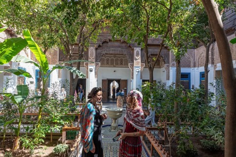 Two woman are talking in the green courtyard of the Bahia Palace with traditional architecture