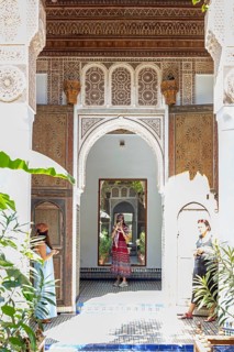 A traditional courtyard with arches, mirrors and decoration and two woman, Bahia Palace in