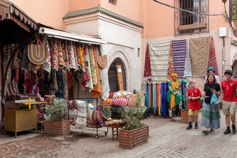Small street full of colorful textiles in a Moroccan bazaar surrounded by visitors