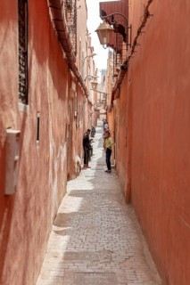 Narrow alley with red walls and walkers on the paved path in an old town