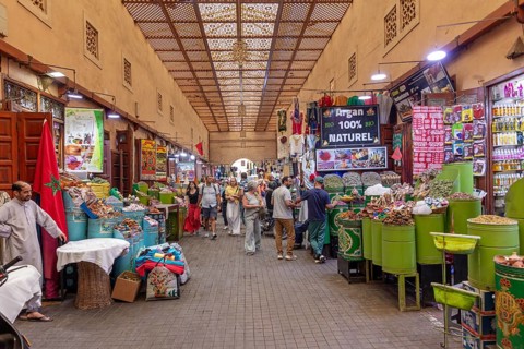 Lively market with numerous stalls full of fruit and goods under a decorative roof