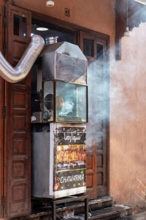 A grill outside a door that emits smoke, probably for preparing street food at night